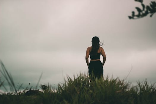 暮光下，一个女人站在多云天空下的草地上，剪影唤起孤独