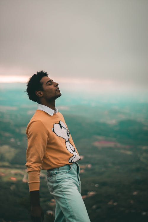 Man in orange and White Sweater Standing on Top of Mountain