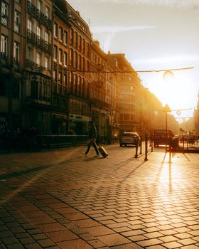 Silhouetted pedestrians and cars on a cobblestone street at sunset in a European city.