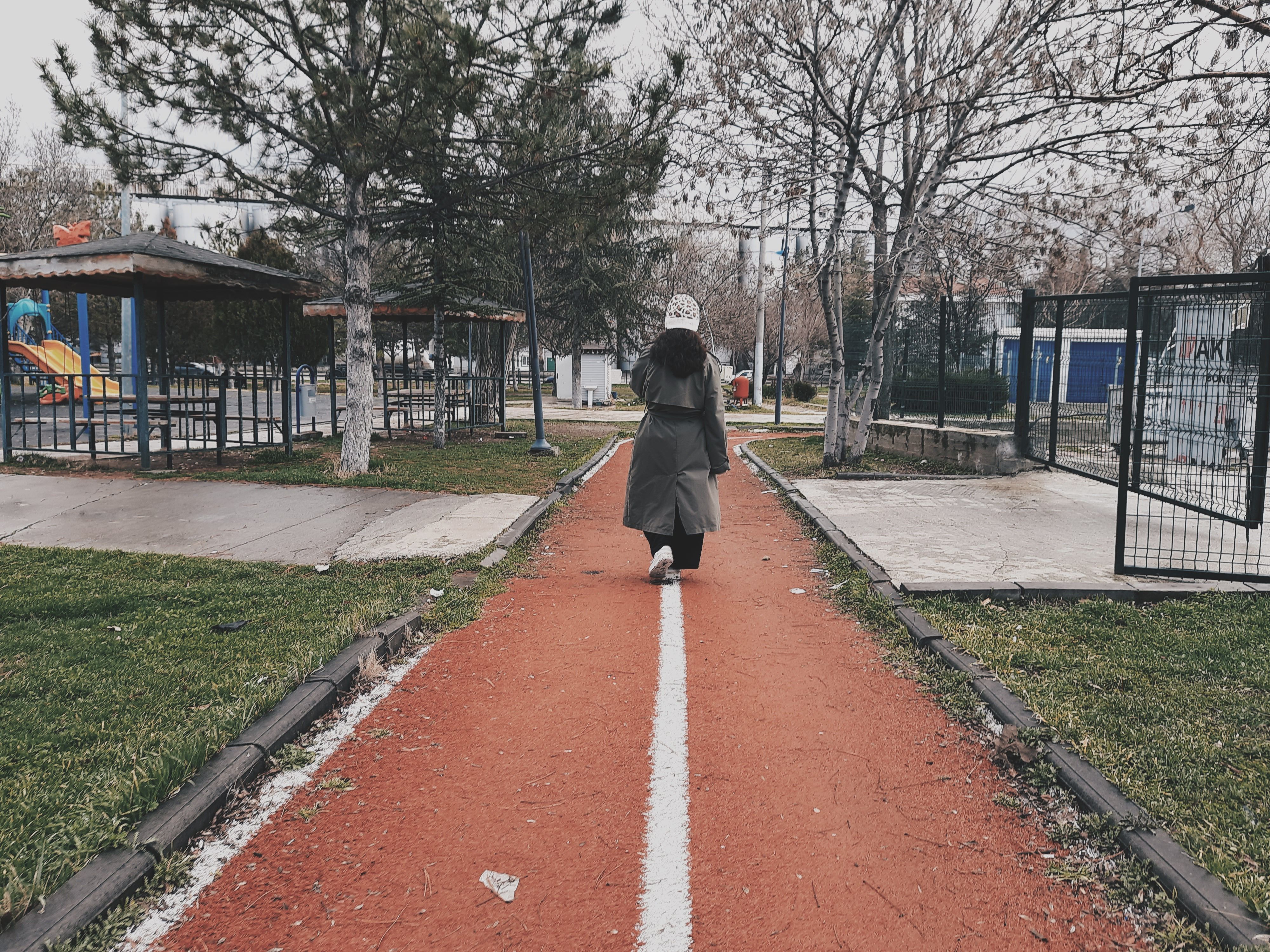 A woman walks along a park path lined with trees in a winter setting.