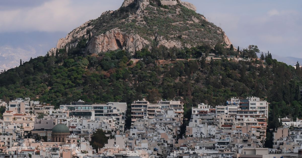 Aerial view of Mount Lycabettus overlooking Athens cityscape under a cloudy sky.
