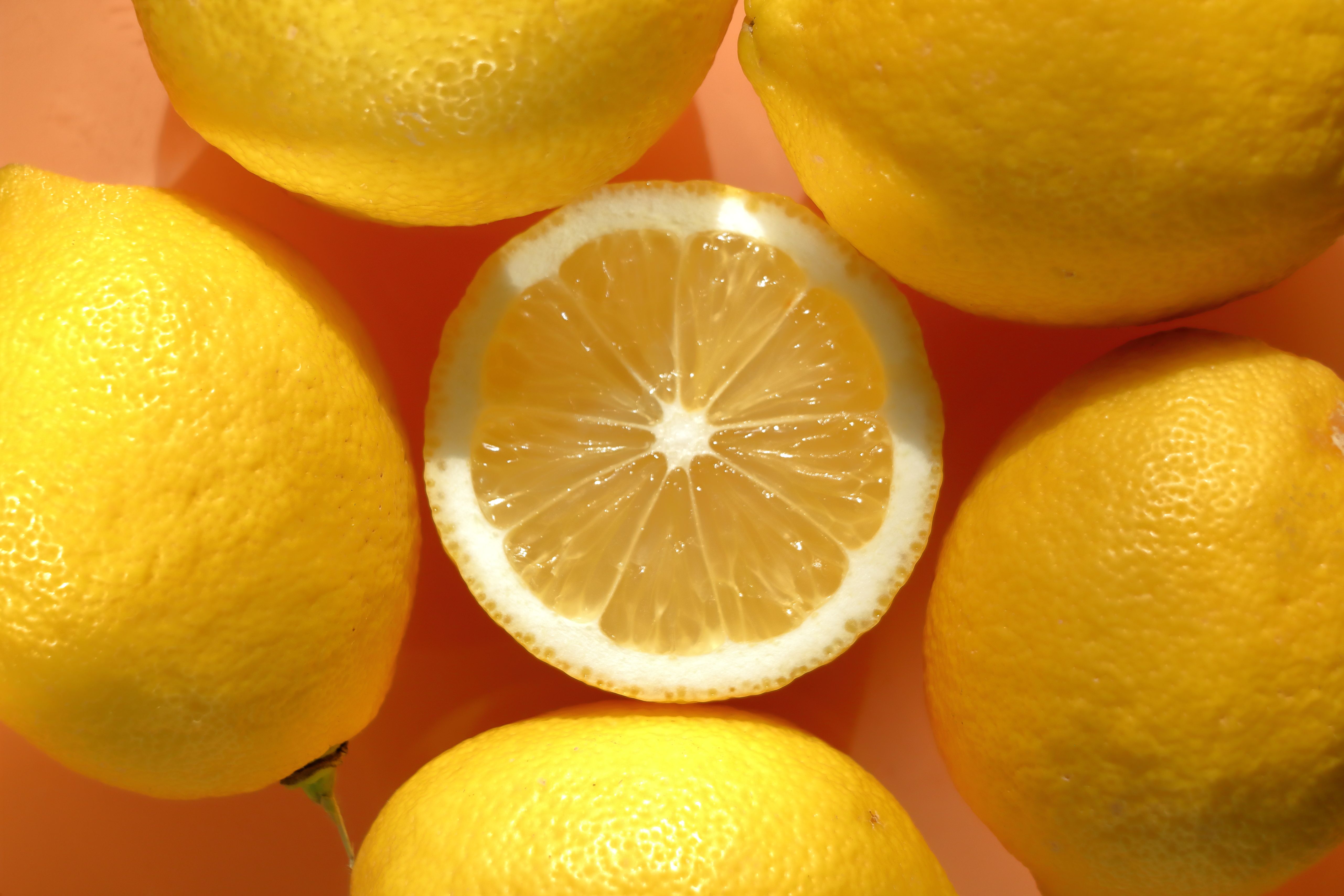 Bright yellow lemons centered around a half slice on a vibrant orange backdrop.