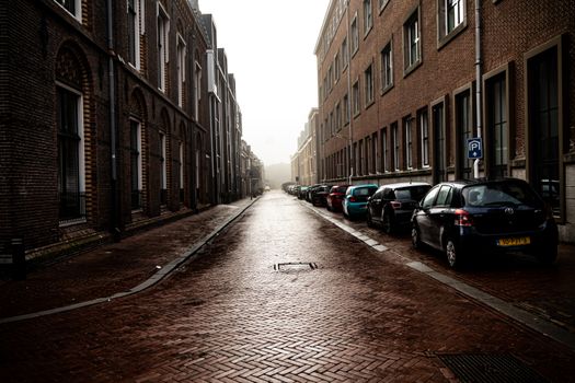 A quiet urban street lined with parked cars and historic brick buildings in the early morning mist.