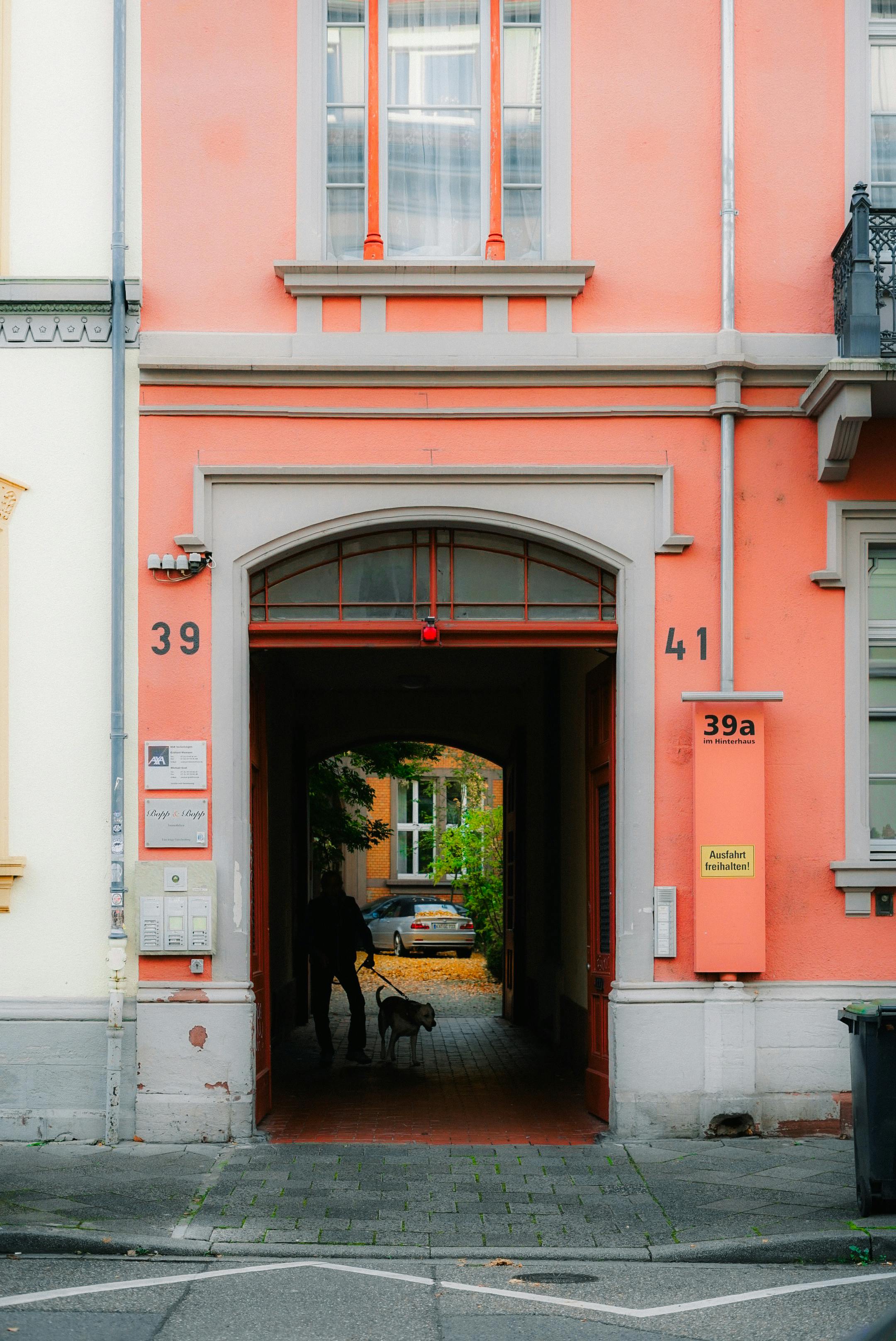 Gratis Hombre paseando a su perro a través de un arco colorido en una ciudad europea, capturando la vida urbana. Foto de stock