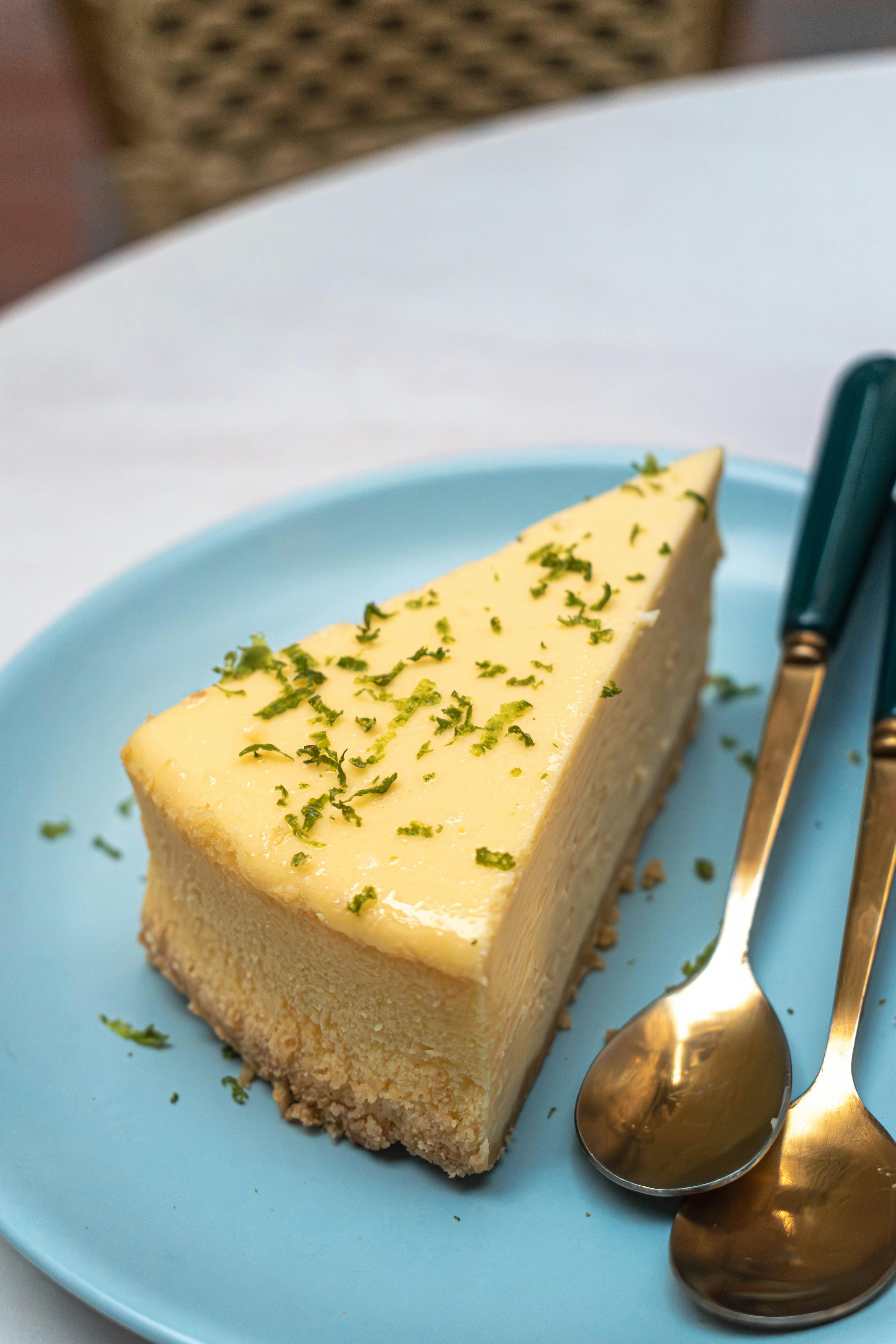 A tempting slice of lime cheesecake topped with zest, served on a blue plate.