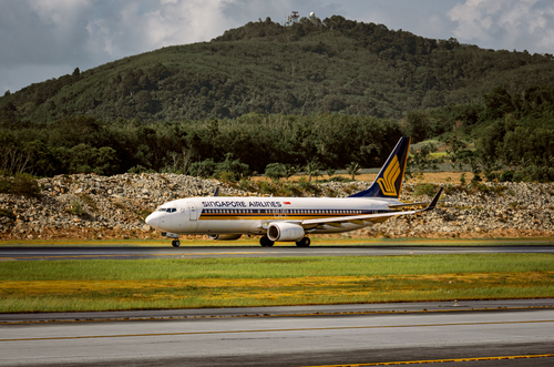 Free A Singapore Airlines plane taxis on the runway against lush hills, showcasing travel and aviation. Stock Photo