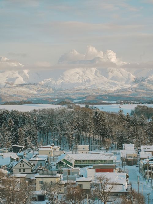 Free A breathtaking aerial view of a snow-covered town with mountain backdrop in Hokkaido, Japan during winter. Stock Photo