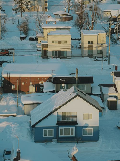 Free Aerial view of snow-covered homes in a Hokkaido village during winter, showcasing serene beauty. Stock Photo