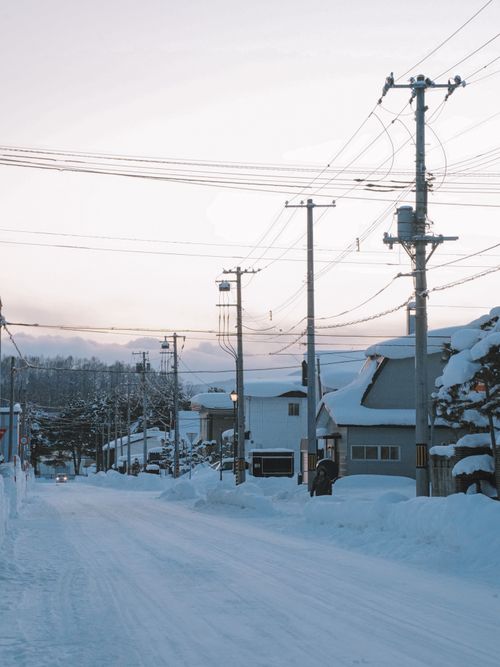 Free Peaceful winter street scene in a snowy Hokkaido town at dusk with telephone lines and snow-covered houses. Stock Photo