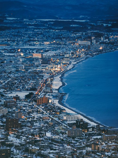 Free Aerial view of a snowy cityscape by the sea in Hokkaido, Japan during night time. Stock Photo