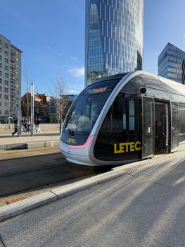 A sleek tram in a bustling cityscape surrounded by tall skyscrapers under a clear blue sky.