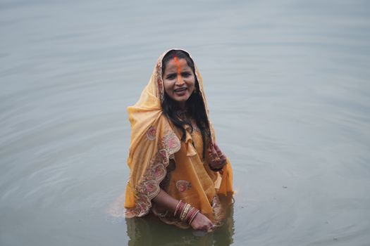 A woman in traditional attire stands in water during a Hindu ritual, exuding cultural richness.