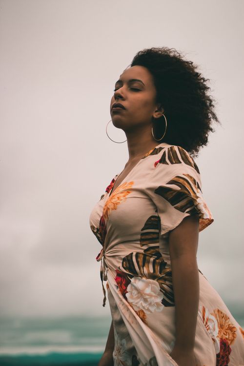 Free Portrait of a woman in a floral dress standing with closed eyes outdoors. Stock Photo
