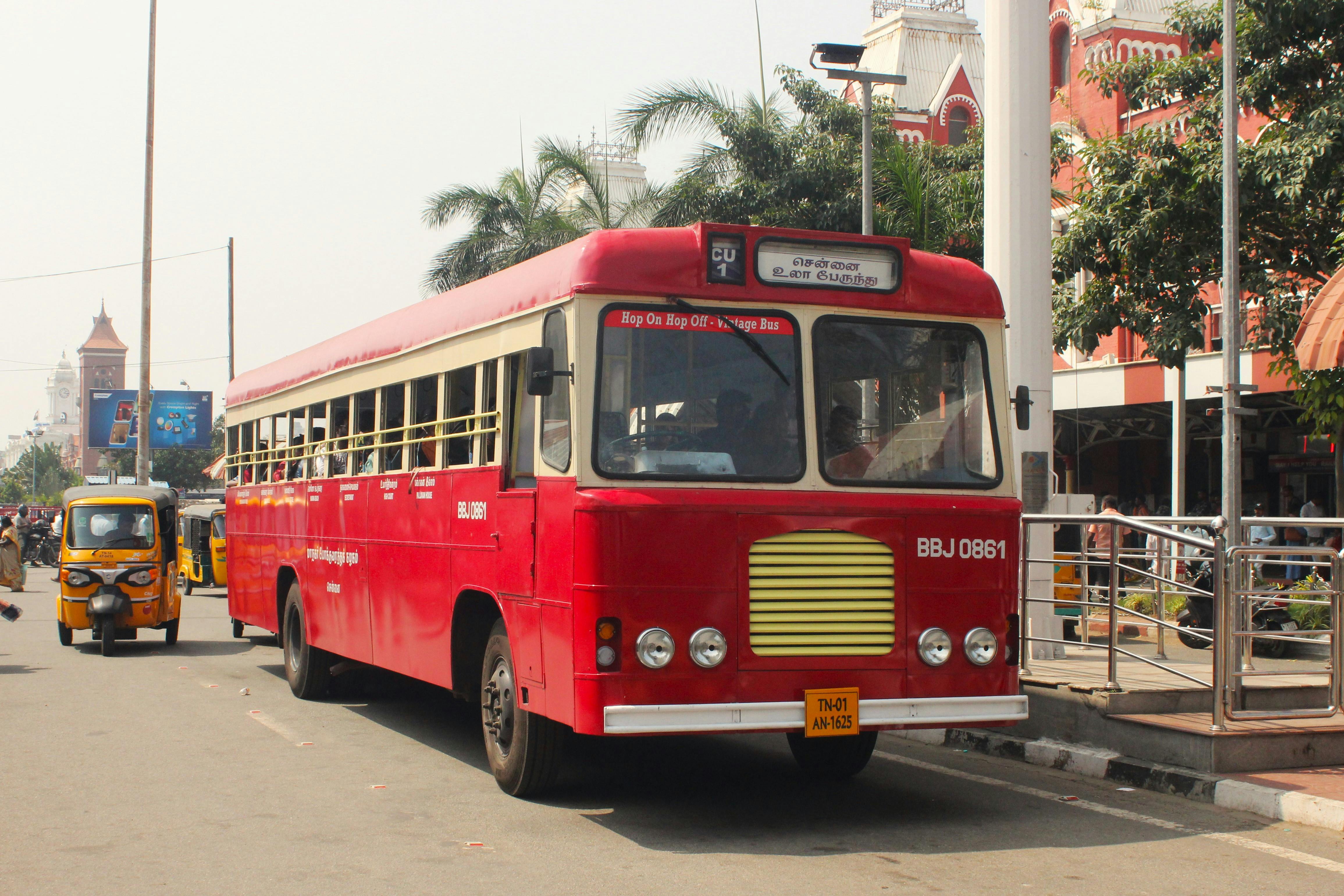 A classic red tour bus in Chennai offering hop-on hop-off services, with vibrant urban scenery.