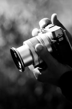 Black and white close-up of hands gripping a vintage camera showing intricate lens details.