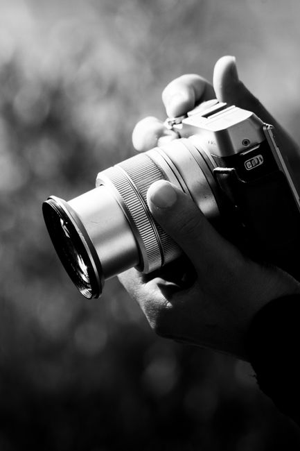 Black and white close-up of hands gripping a vintage camera showing intricate lens details.