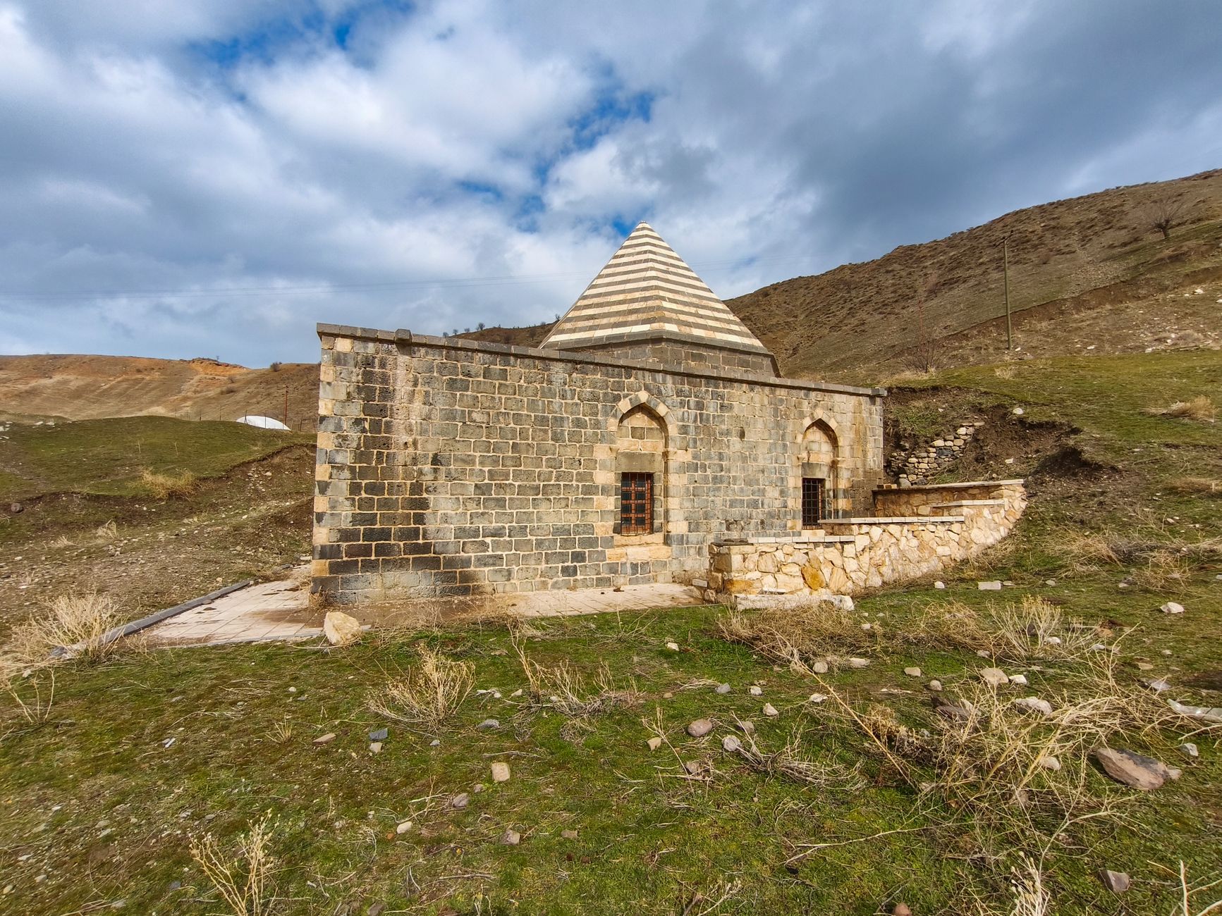 Ancient stone structure in Palu, Elazığ, Türkiye's rural landscape with cloudy skies.