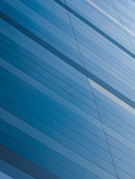 现代蓝色玻璃建筑立面的抽象视图中，几何线条反射着阳光