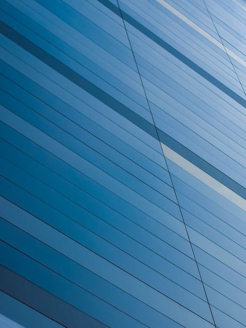 Abstract view of a modern blue glass building facade with geometric lines reflecting sunlight.