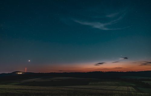 Free A serene night sky with stars illuminating a calm countryside scene with distant hills. Stock Photo