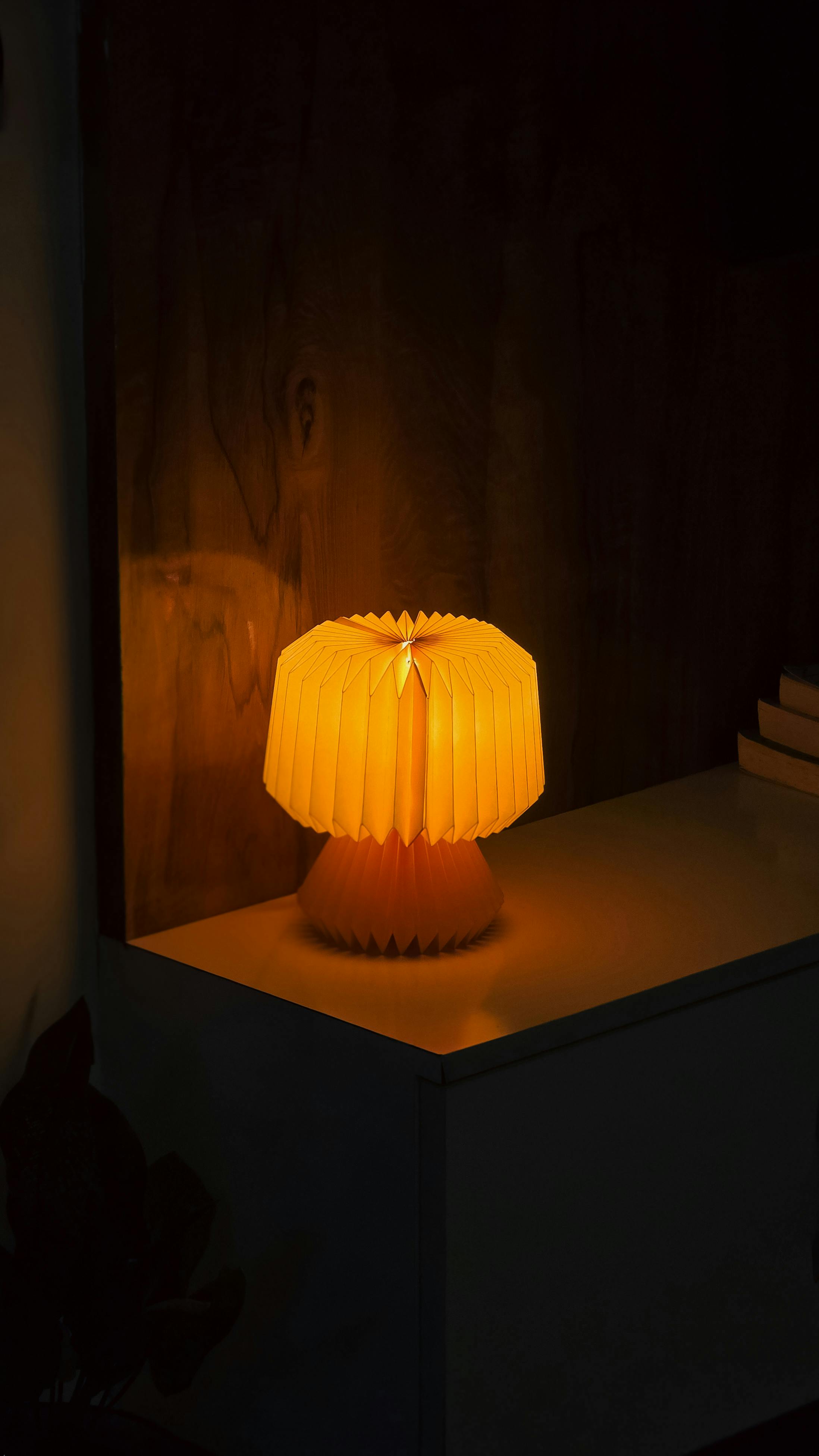 Kostenlos Eine leuchtende Tischlampe wirft warmes Licht auf einen Nachttisch in einem schwach beleuchteten Zimmer. Stock-Foto