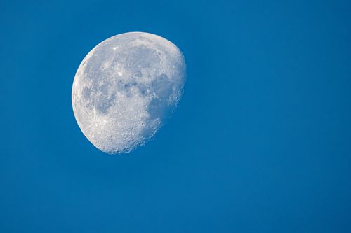 Free Detailed photo of the Moon's surface against a vibrant blue sky, highlighting lunar craters. Stock Photo