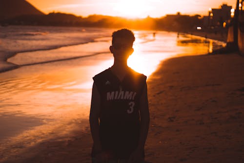 Человек в черном жилете, стоящий на пляже во время заката