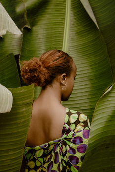A woman in a colorful dress is framed by lush banana leaves.
