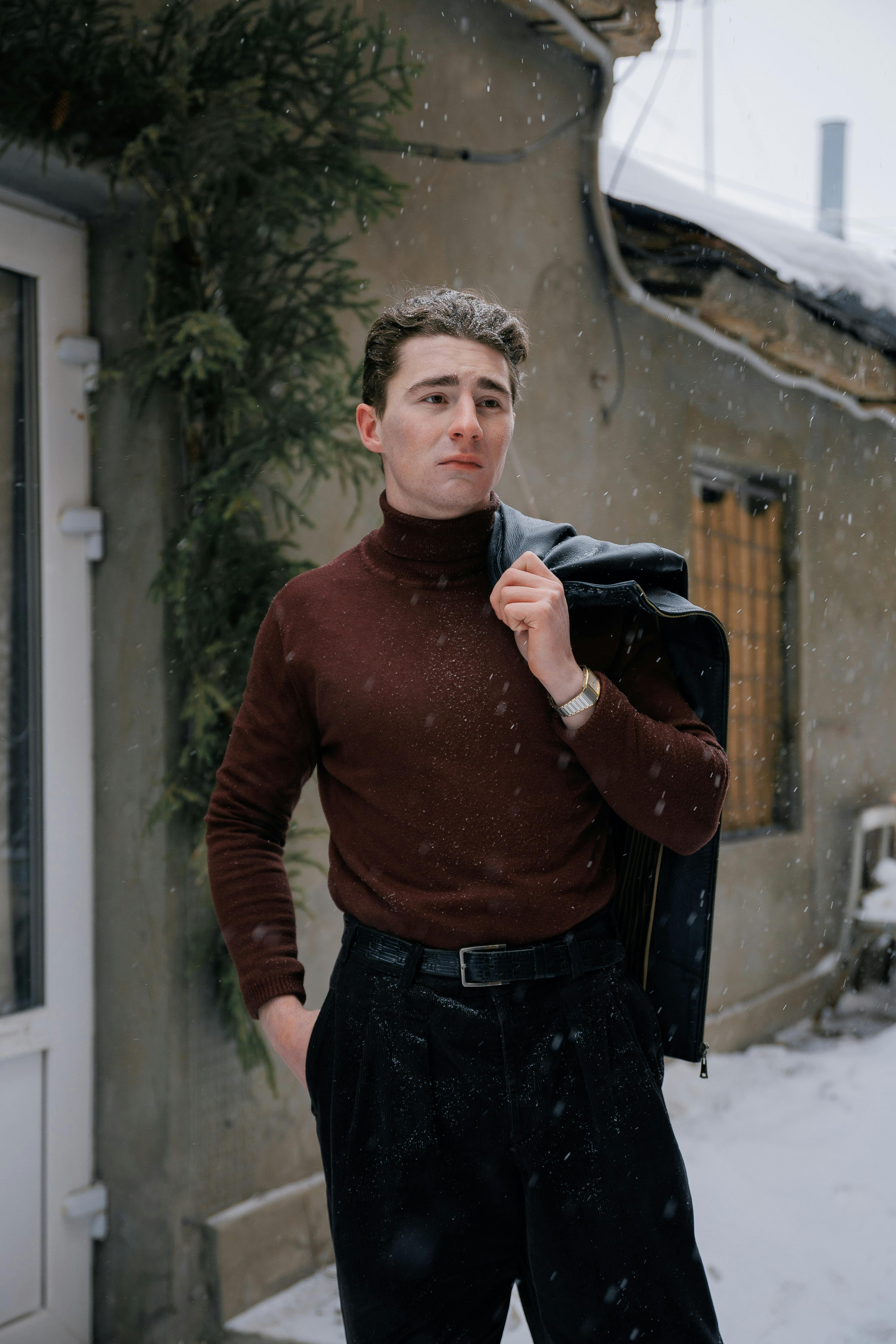 Free Stylish young man in a turtleneck standing outside in winter snow holding a jacket. Stock Photo