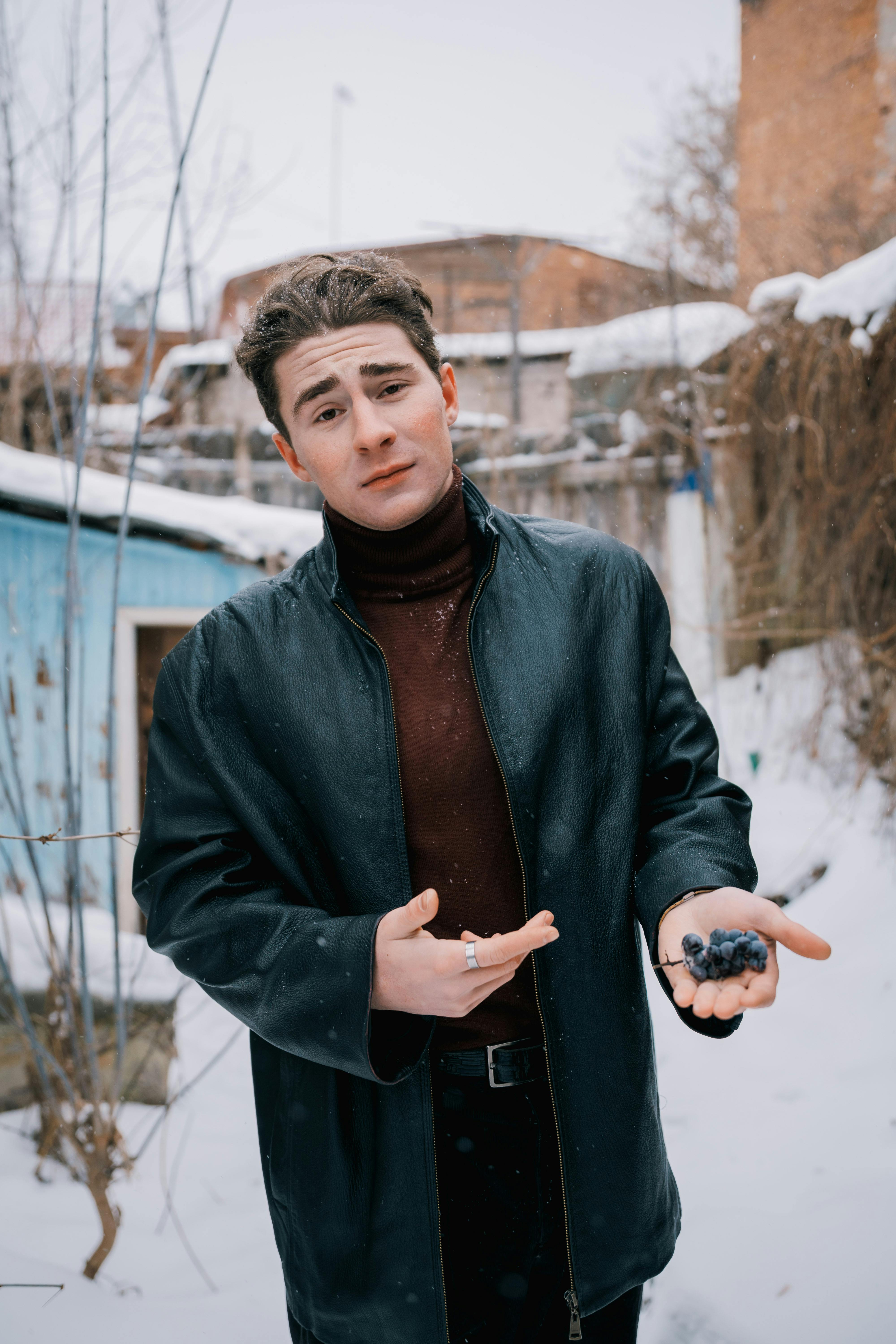 Bezpłatne Młody mężczyzna stoi na zewnątrz w zimowym śniegu, trzymając w ręku kiść winogron. Zdjęcie z galerii