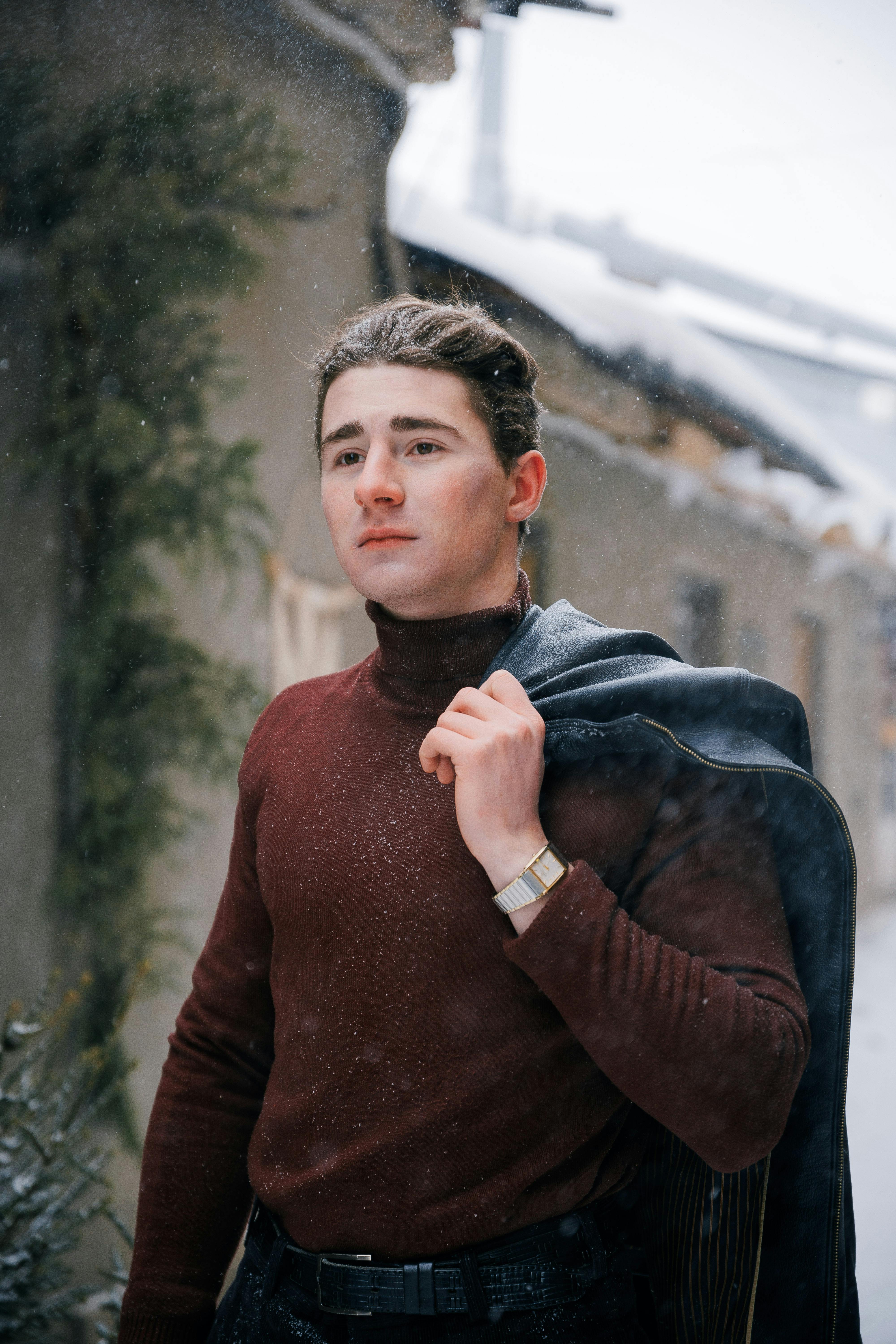 無料 冬の服装をした若い男性が、雪の降る都会の風景の中で自信に満ちたポーズをとっています。 写真素材