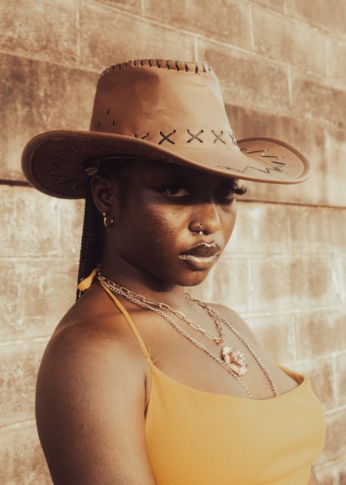 Free Confident woman wearing a brown cowboy hat against a neutral wall backdrop. Stock Photo