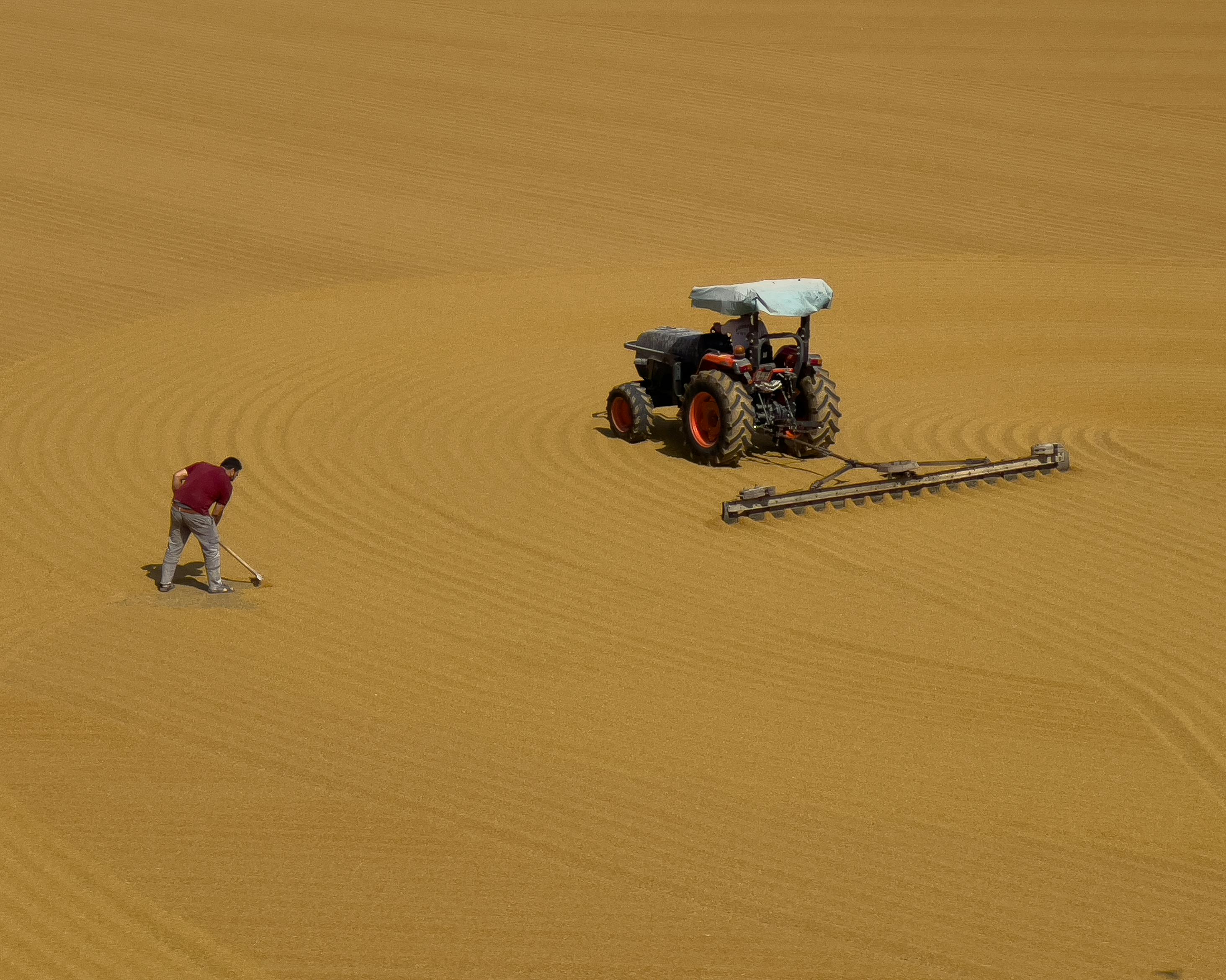 Aerial view of a man and tractor in a wheat field, creating patterns.