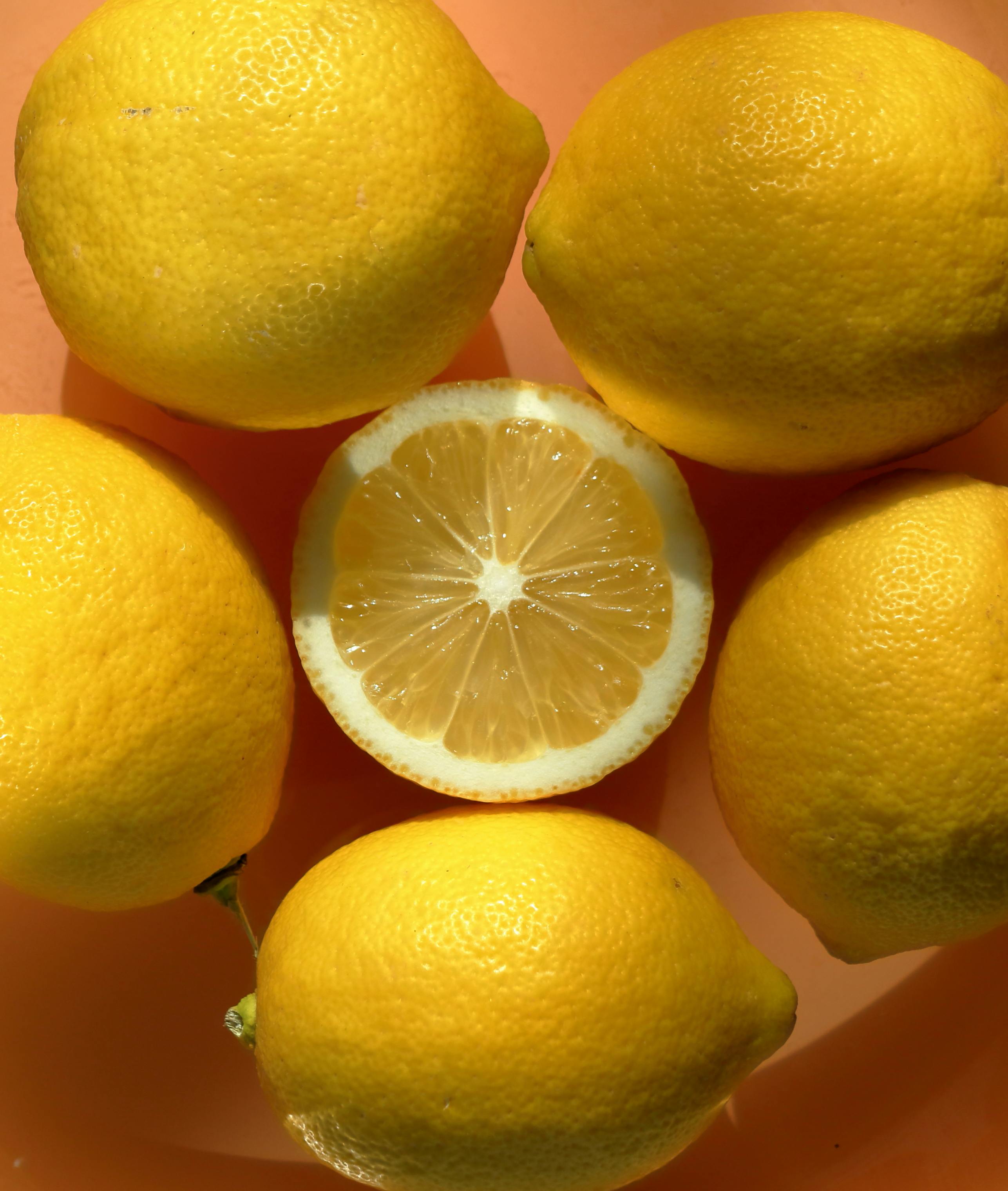 ingyenes Élénk narancssárga felületre helyezett citromok magas szögből, érett citrusféléket bemutatva. Stockfotó