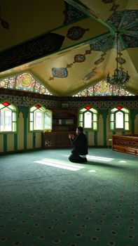 A man praying in a beautifully decorated mosque with stained glass windows in İstanbul.