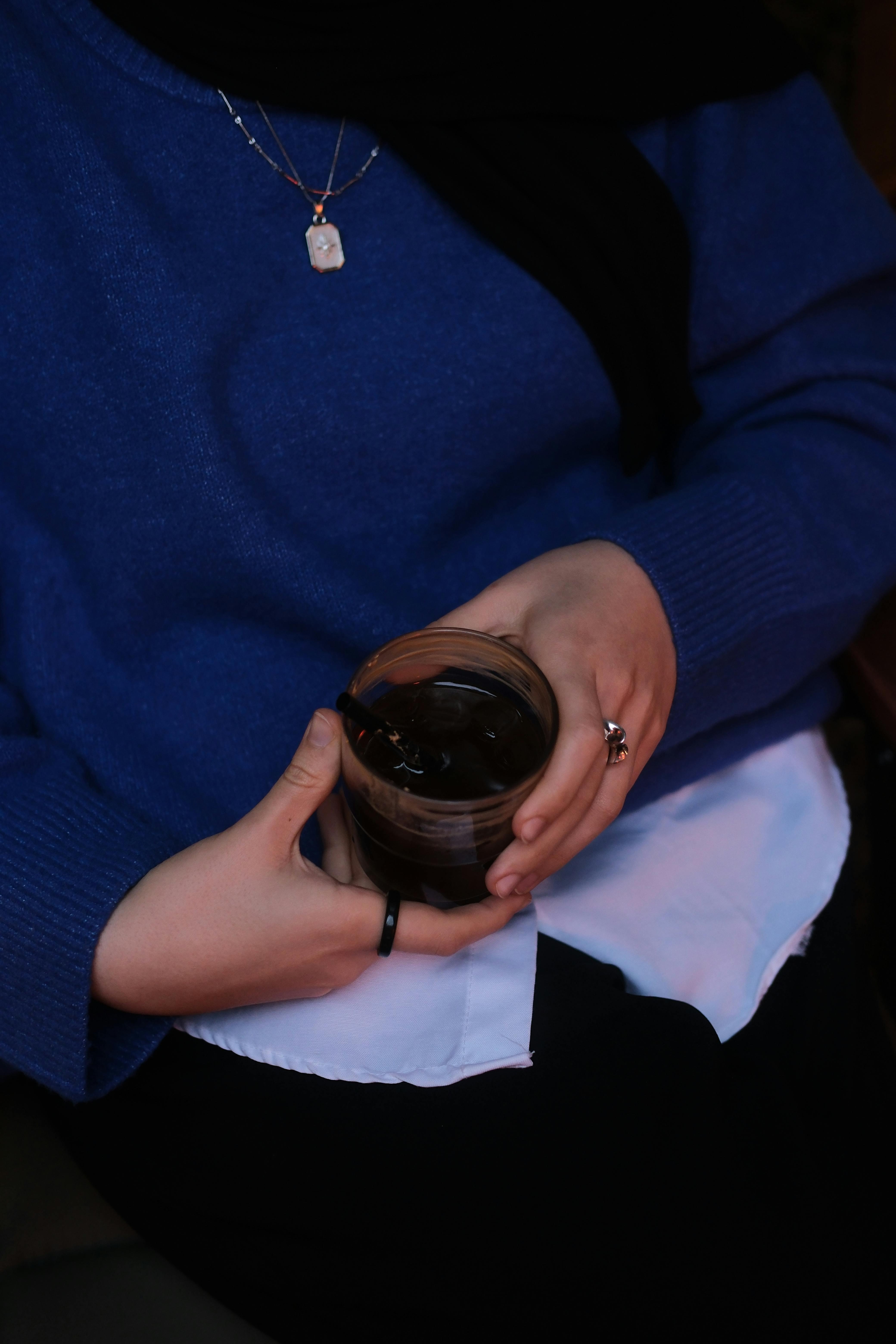 gratis Gezellige scène van een vrouw die in gedempt licht een glas met een drankje vasthoudt, gekleed in een blauwe trui. Stockfoto