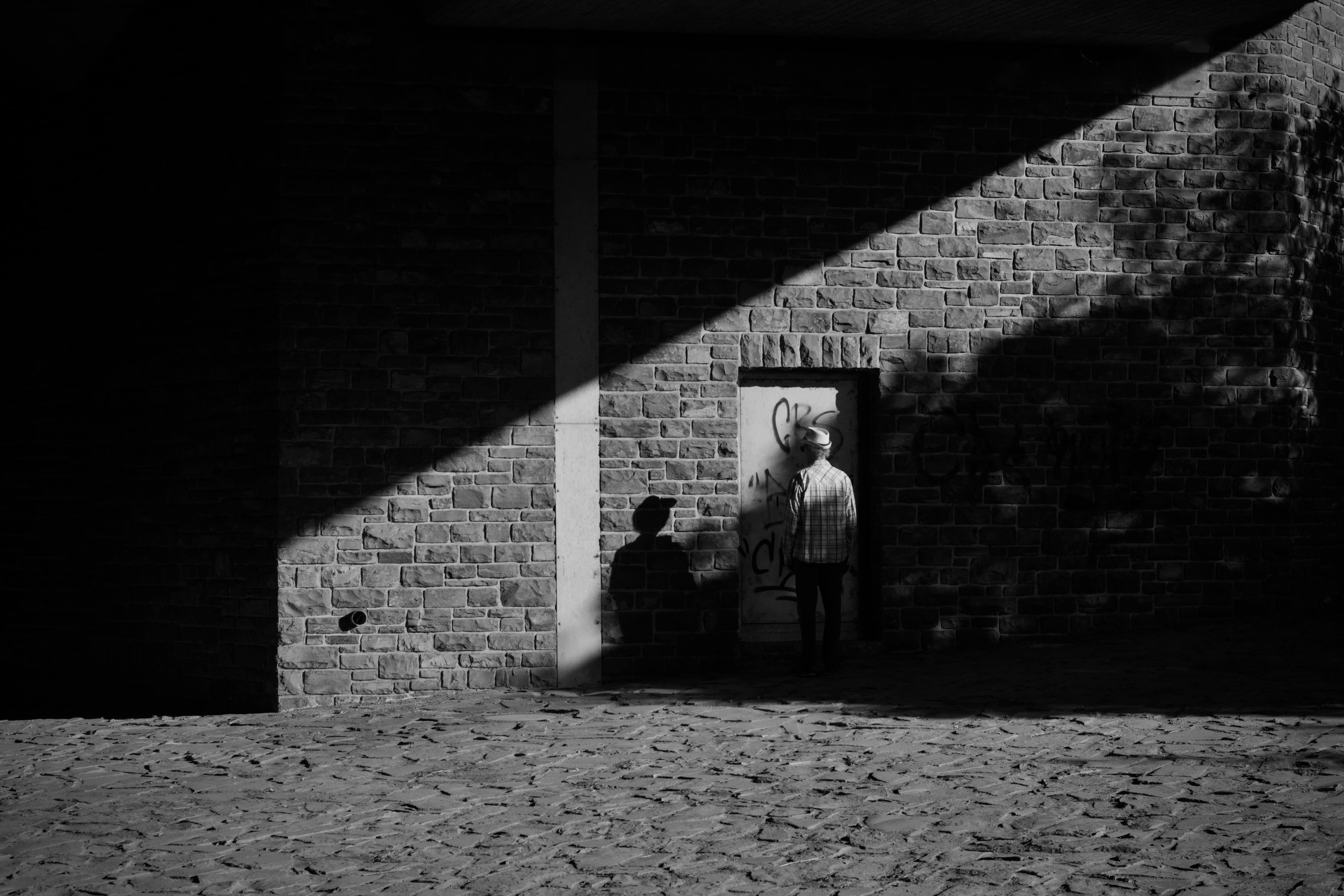 grátis Fotografia em preto e branco de um homem junto a uma parede, projetando sombras dramáticas. Foto profissional