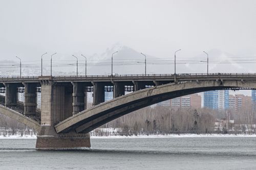 Free A concrete bridge spans a river with snow-capped mountains and cityscape in the background. Stock Photo