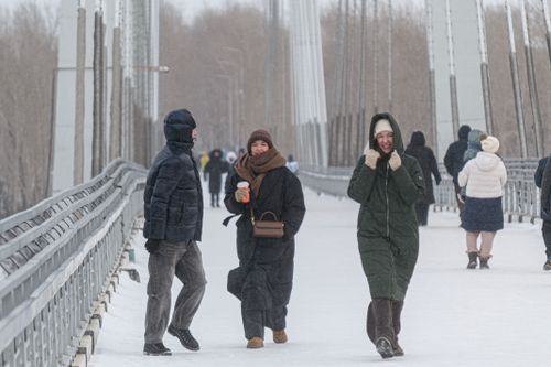 Free People bundled up against the cold walking on a snowy bridge in winter. Stock Photo