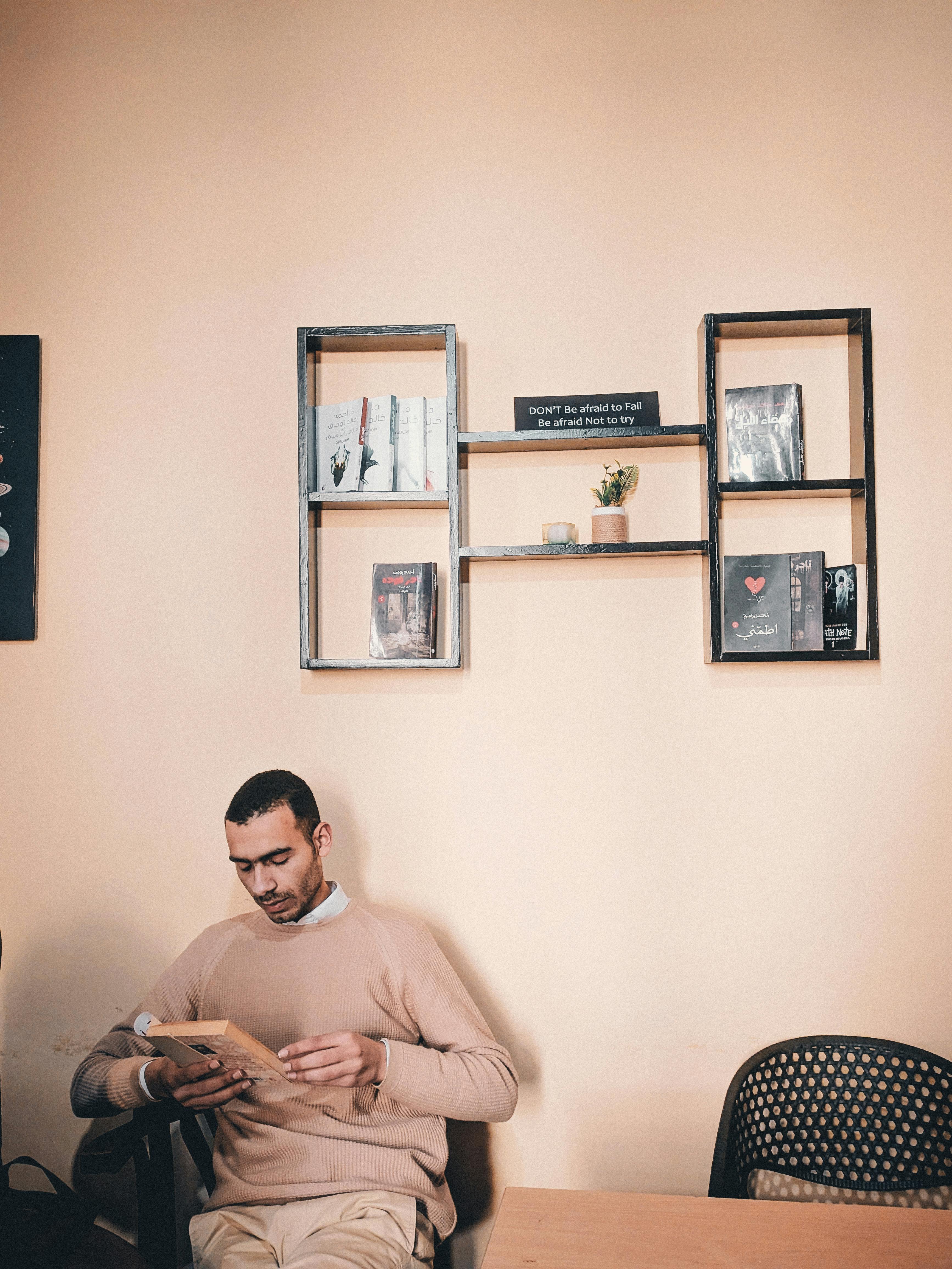 Ücretsiz Evindeki şık bir çalışma odasında, dekoratif raflarla çevrili bir ortamda kitap okuyan yetişkin bir adam. Stok Fotoğraflar