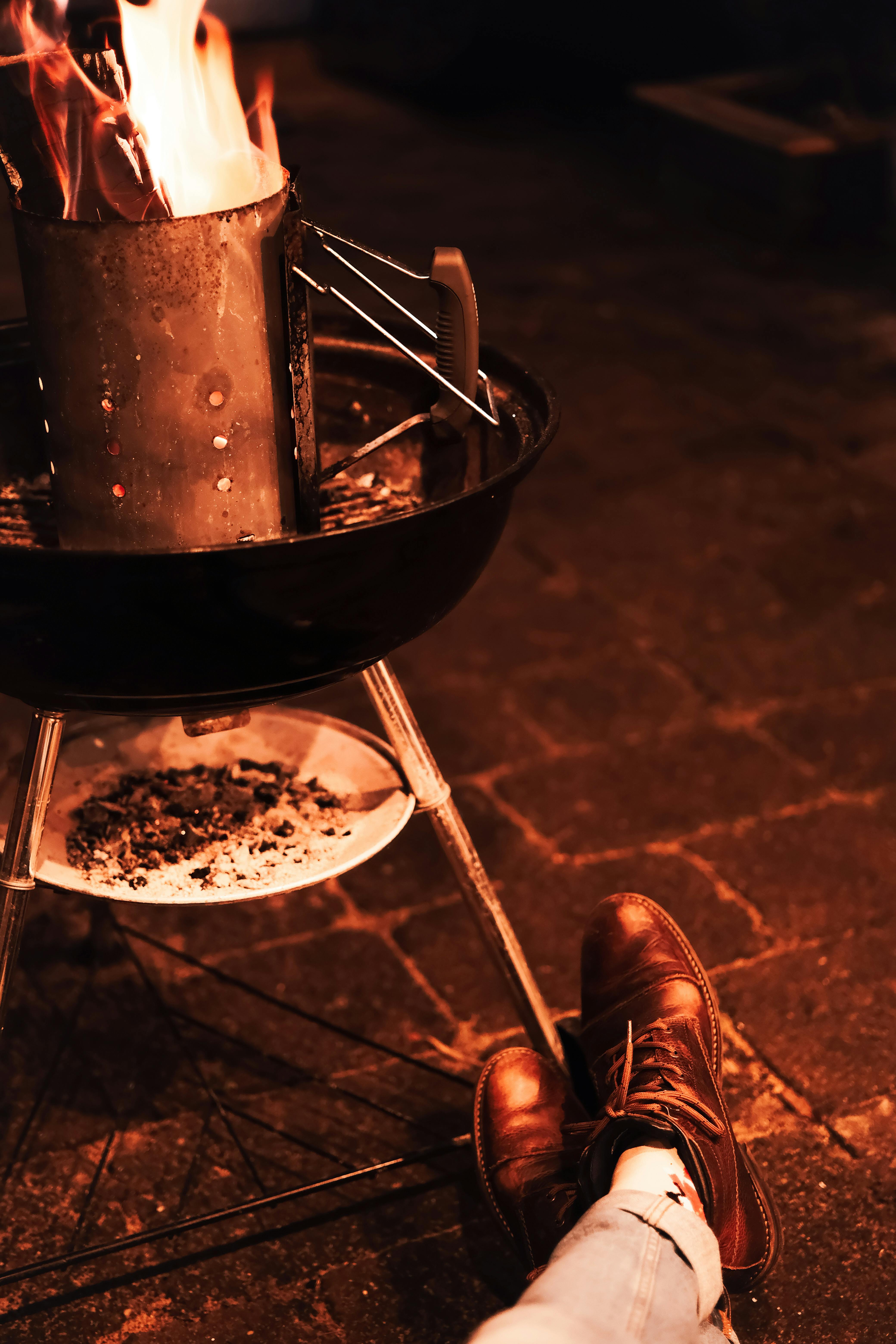Free Warm evening fire in a grill with boots resting on the pavement, creating a cozy outdoor ambiance. Stock Photo