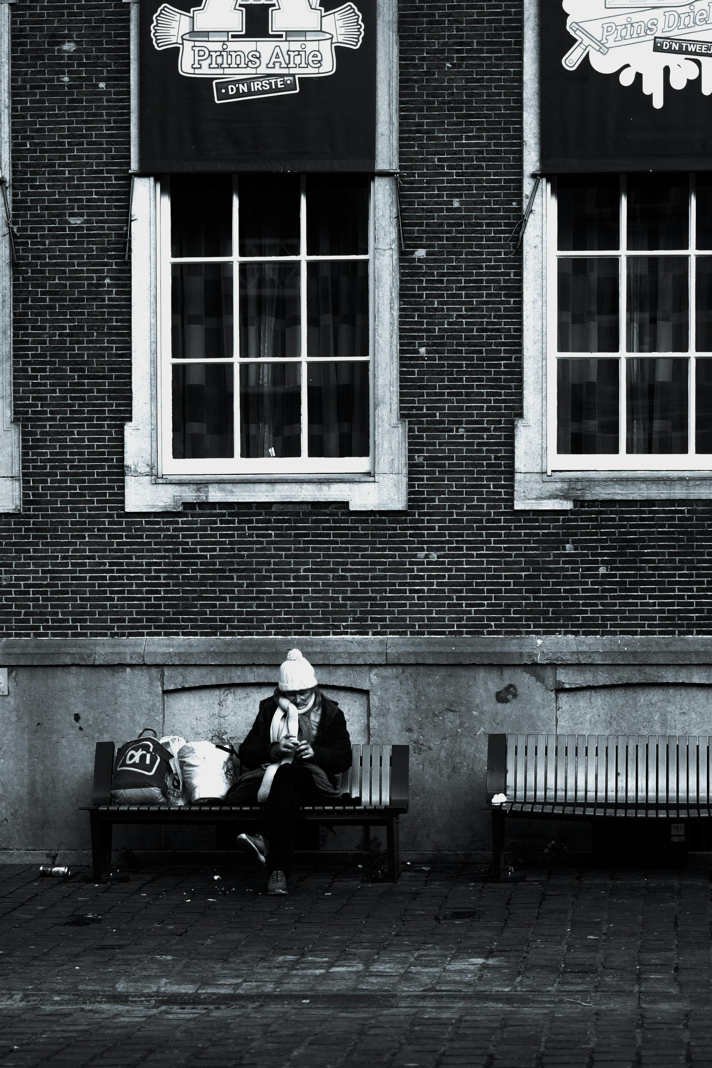 De franc Persona asseguda sola en un banc a la ciutat, envoltada de parets de maó, invocant una sensació de solitud. Foto d'estoc