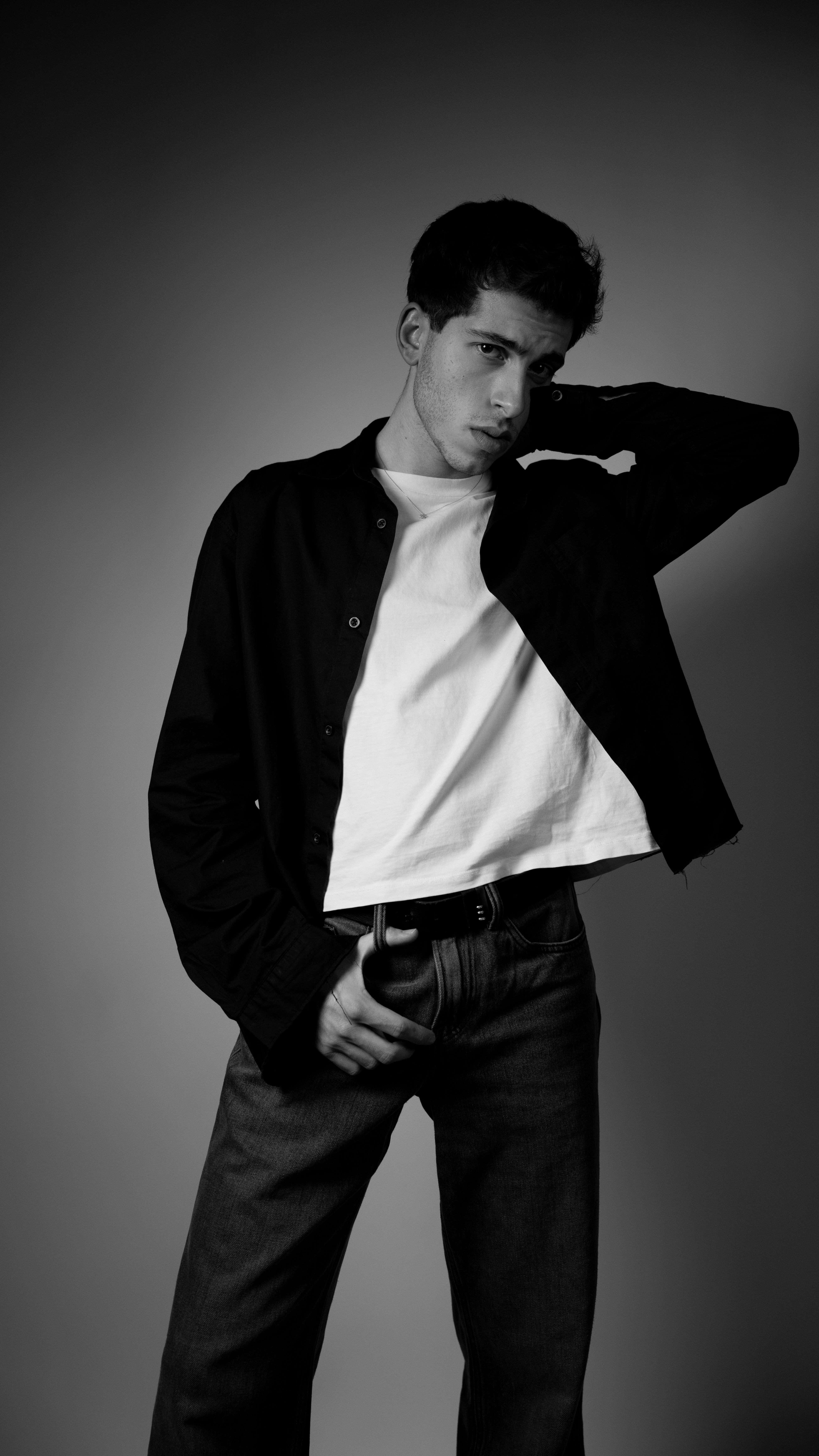 Stylish black and white portrait of a young man posing confidently in a studio setting.