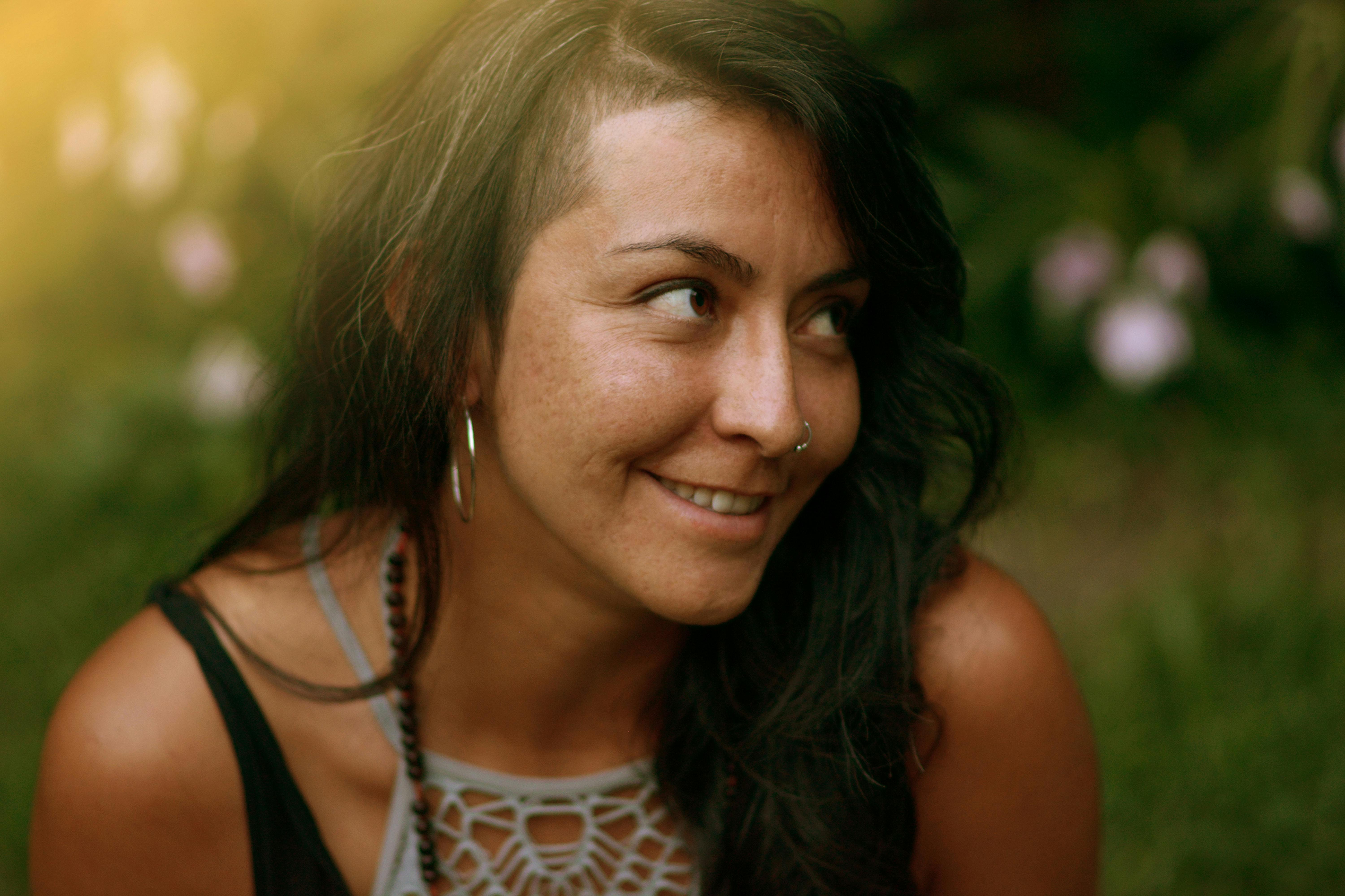 grátis Retrato de uma mulher alegre, de longos cabelos escuros, sorrindo ao ar livre em um jardim ensolarado. Foto profissional