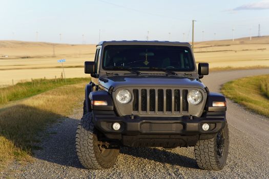 Front view of a Jeep Wrangler on a gravel road in a rural Canadian landscape with wind turbines.