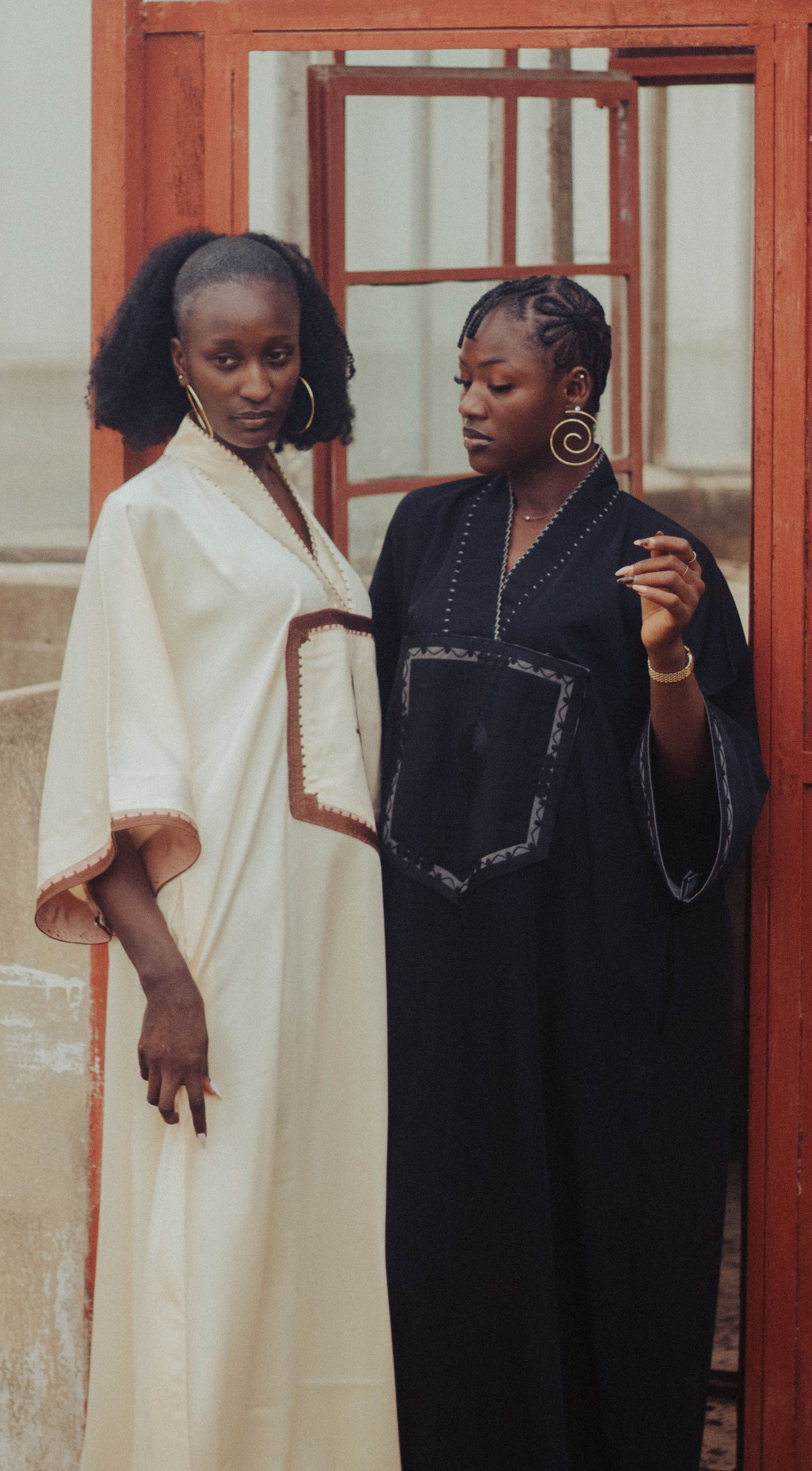 Two women in stylish traditional dresses stand gracefully by a vintage door, exuding elegance and poise.