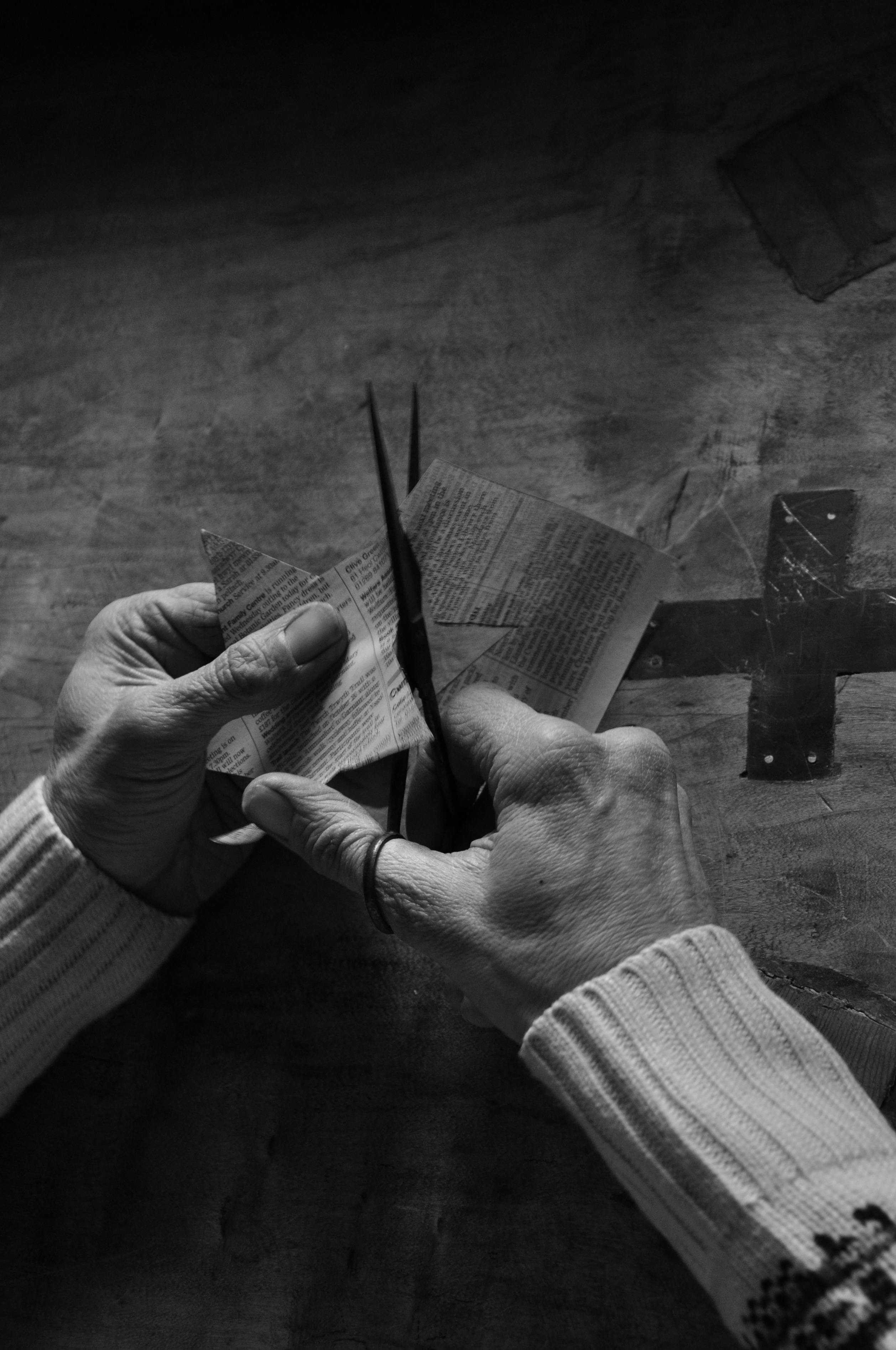 Безкоштовне Чорно-біле зображення рук літніх людей, які займаються рукоділлям з паперу та ножиць, підкреслюючи традиції. стокове фото