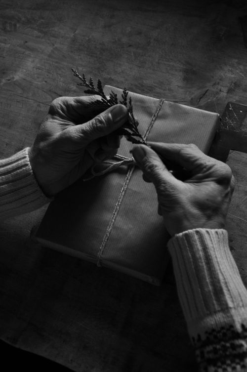 Free A black and white image of elderly hands wrapping a rustic gift with natural materials. Stock Photo