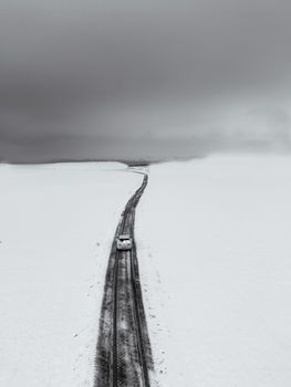 A solitary car travels along a snowy road in Adıyaman, demonstrating visual minimalism and winter's stark beauty.