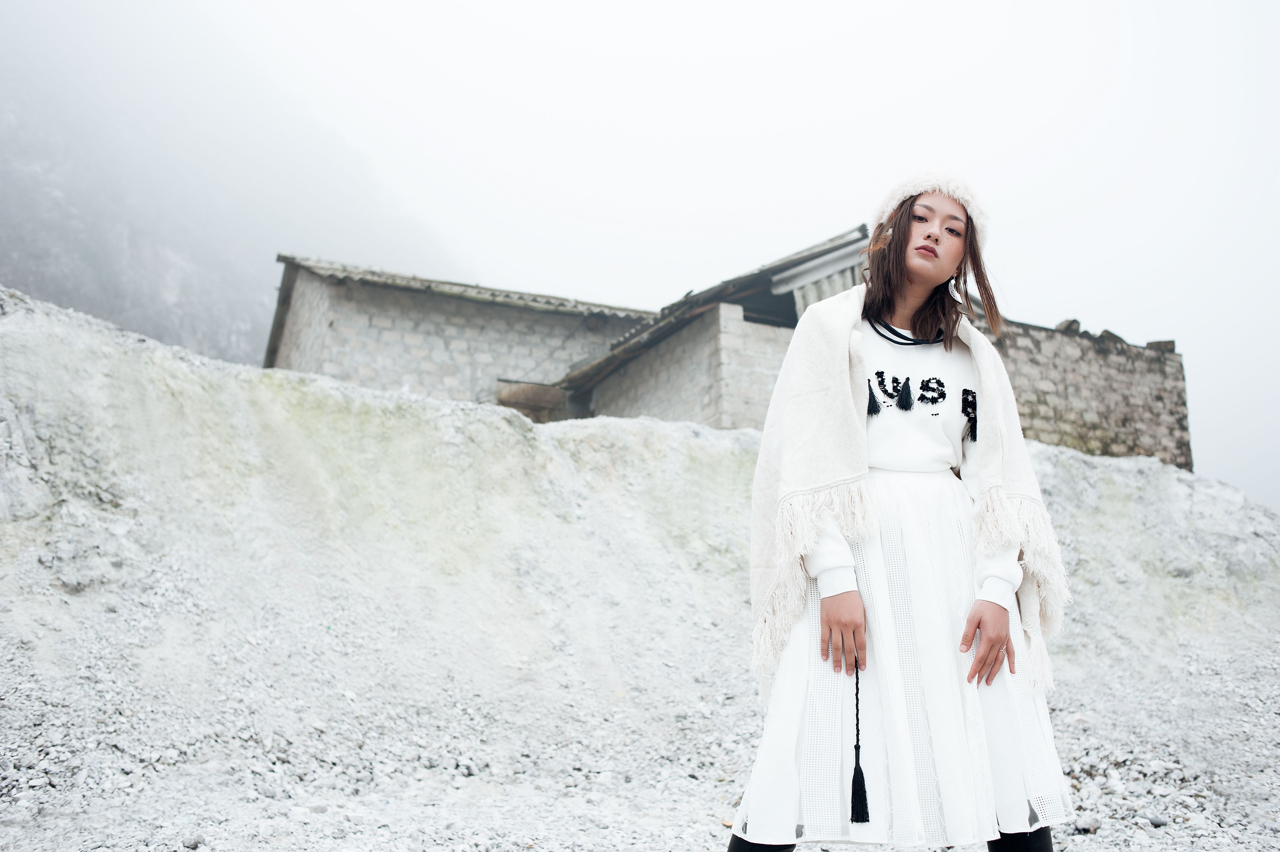 Stylish woman in winter attire standing in snowy mountainous landscape.